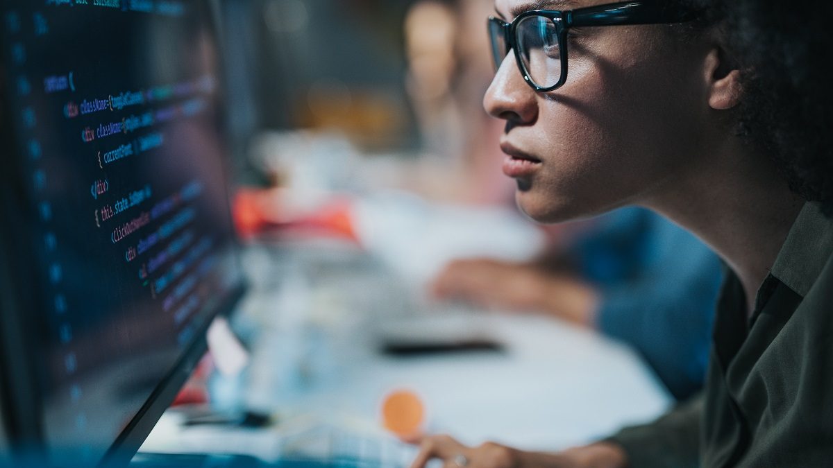 Focused black female programmer coding new computer language while working on desktop PC in the office.