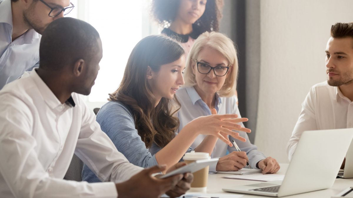 Young female mentor leader coach teaching employees group analyzing online project explaining business strategy speaking training diverse corporate team with laptop using computer at office meeting