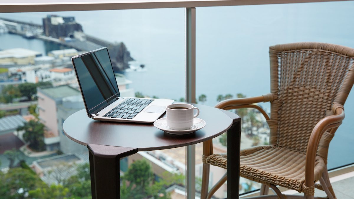 Working from home. Workplace with laptop and cup of coffee on balcony overlooking ocean.