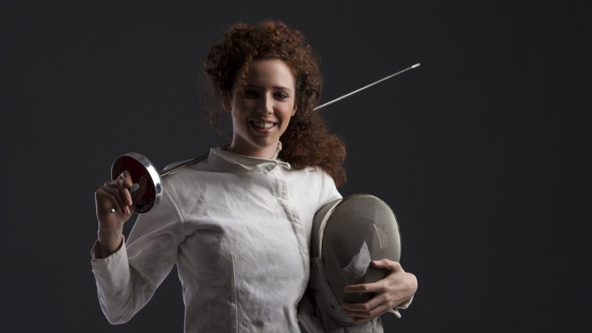 Fencing sport competition. Dark grey background. Sporting Women. Portrait curly redhead girls fencer.