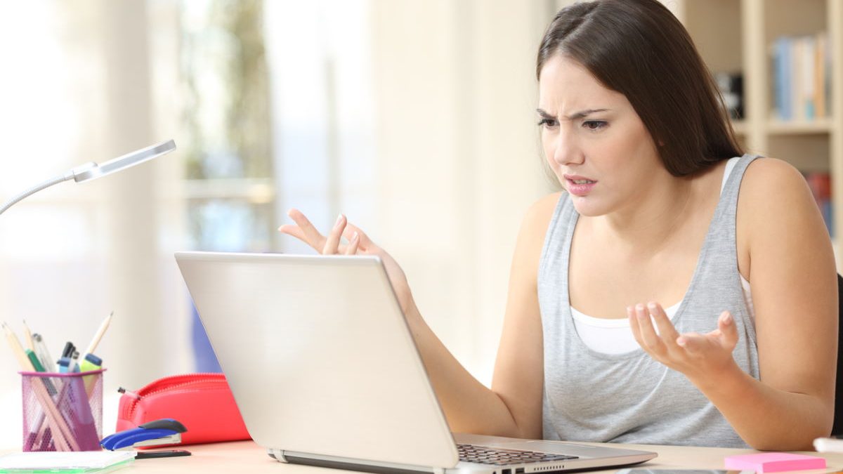 Angry student looking at laptop on a desk at home