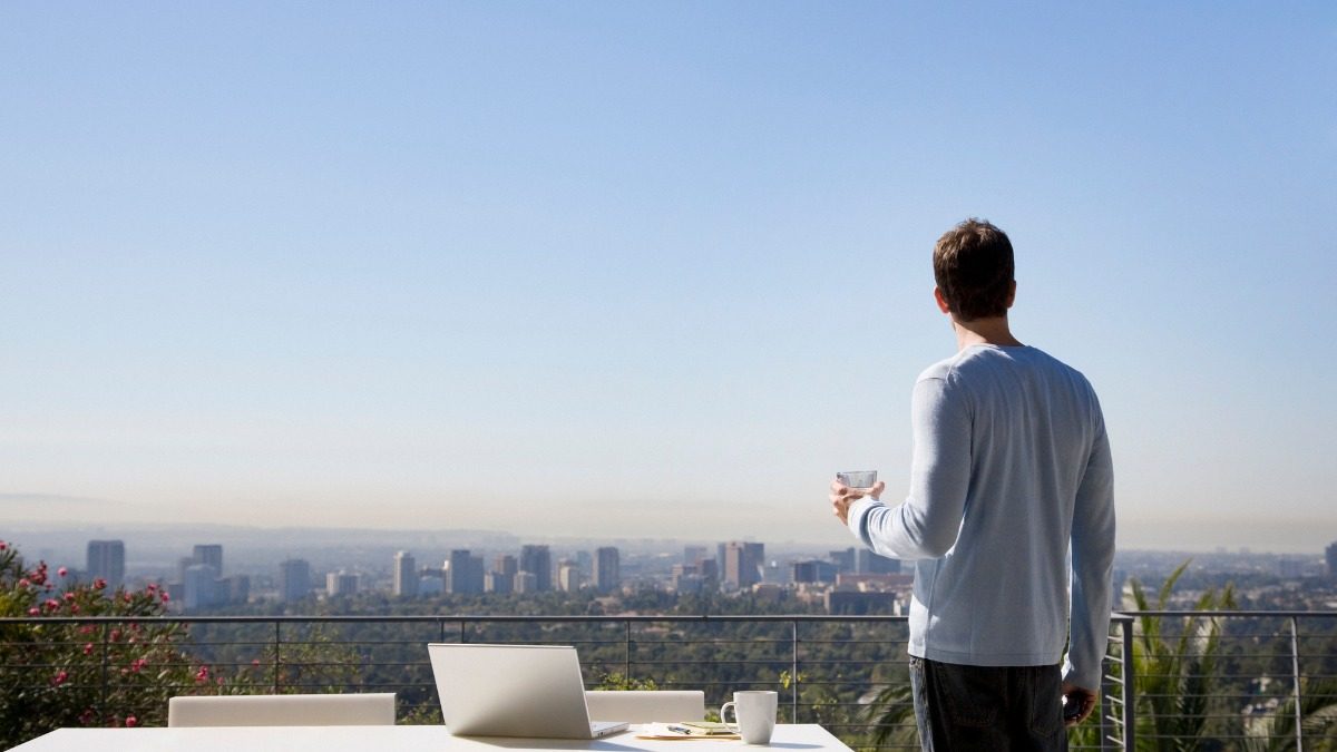 man-using-laptop-on-balcony-overlooking-city-picture-id88621587